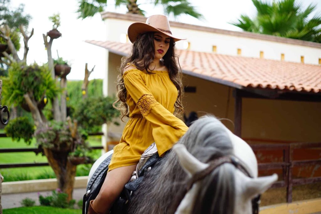 Girl in yellow dress and tan cowboy hat riding a grey horse